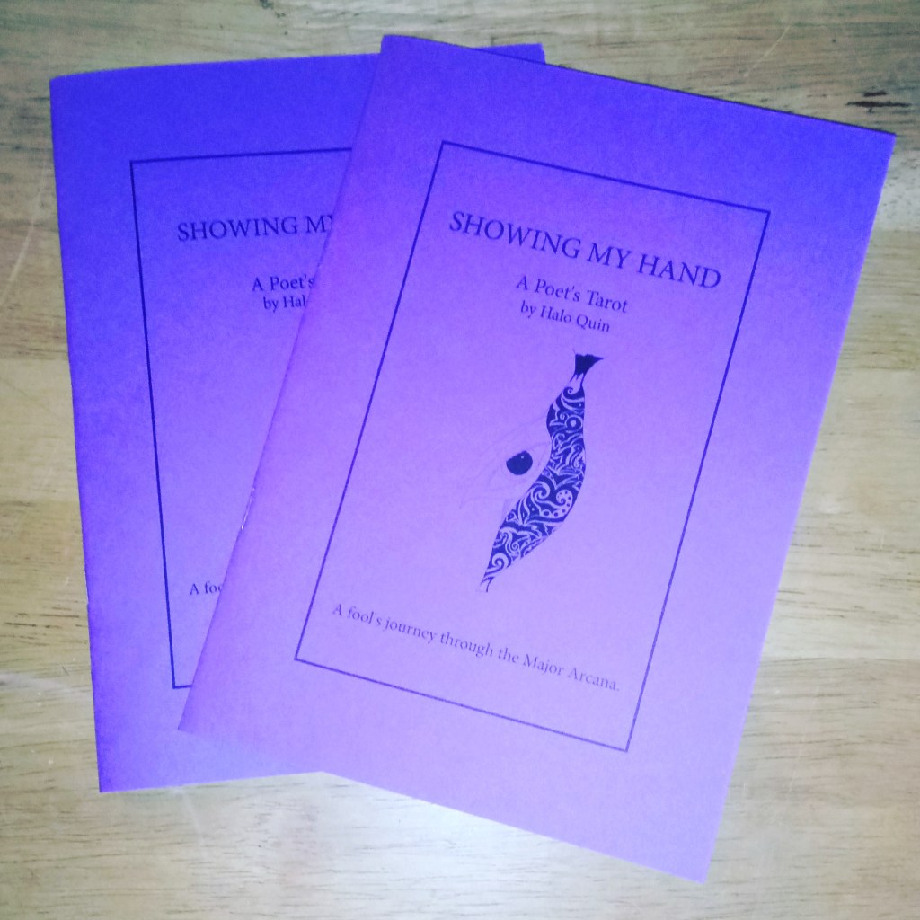 Two violet booklets with a butterfly emerging from a crysalis depicted on the cover, on a wooden surface. Title: "Showing My Hand: a Poet's Journey through the Tarot by Halo Quin".